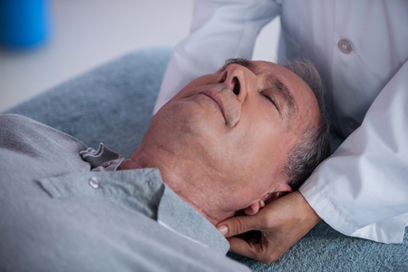 Senior man receiving neck massage from physiotherapist in clinicの写真素材