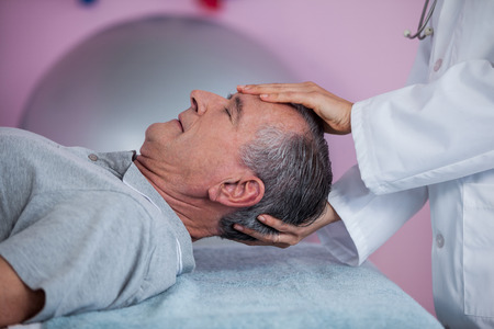 Senior man receiving head massage from physiotherapist in clinicの写真素材