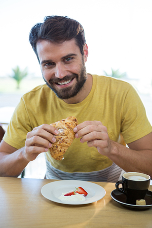 Portrait of smiling man having croissant in coffee shopの写真素材