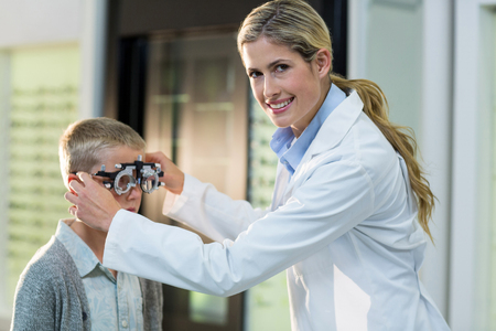 Female optometrist examining young patient with phoropter in ophthalmology clinic