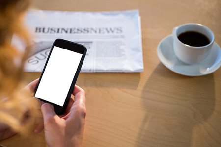 Mid section of woman using her mobile phone with newspaper and coffee cup on tableの写真素材