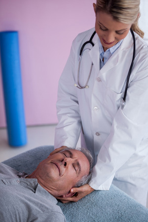 Senior man receiving neck massage from physiotherapist in clinicの写真素材