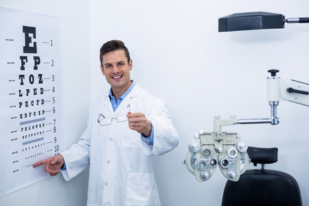 Handsome optometrist pointing at eye chart in ophthalmology clinicの写真素材