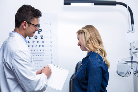 Optometrist discussing eye test report with female patient in ophthalmology clinicの写真素材