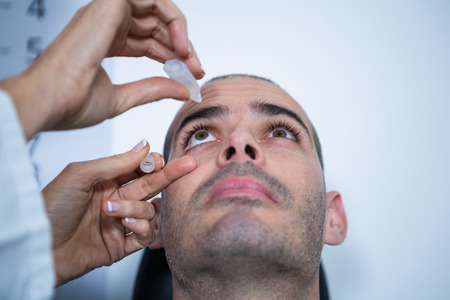 Optometrist putting drops into patients eyes in ophthalmology clinicの写真素材