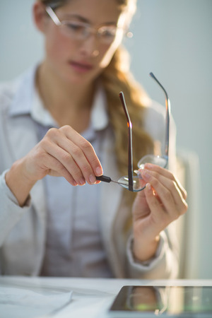 Attentive female optometrist preparing glass frame in ophthalmology clinicの写真素材