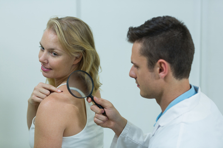 Dermatologist examining mole with magnifying glass in clinicの写真素材