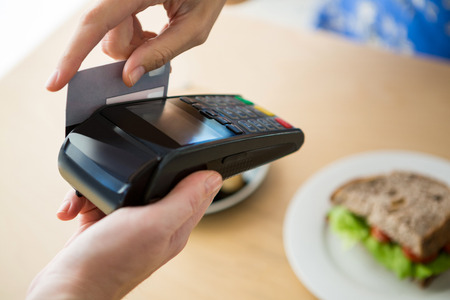 Close-up of hand holding a credit card next to the digital tablet in the coffee shop