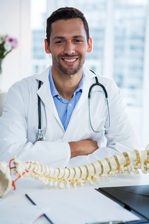 Portrait of smiling physiotherapist sitting with spine model in clinicの写真素材