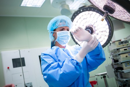 Female surgeon wearing surgical gloves in operation room at hospital