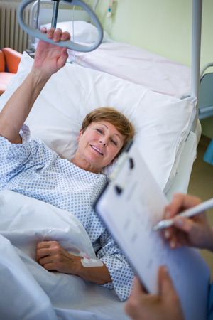 Patient lying on bed while nurse writing on clipboard in hospitalの写真素材