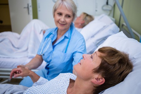 Nurse examining patients pulse in hospital roomの写真素材