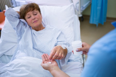 Nurse giving medication to patient in hospital wardの写真素材