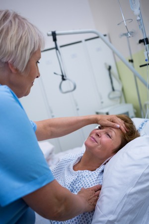 Nurse checking patient temperature in hospital roomの写真素材