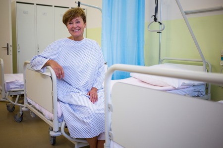 Portrait of smiling senior patient sitting on a bed in hospital roomの写真素材