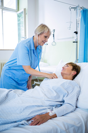 Nurse examining a patient with a stethoscope in hospital wardの写真素材