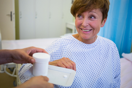 Nurse giving medication to senior patient in hospital roomの写真素材