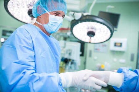 Surgeons shaking hands in operation room at hospitalの写真素材