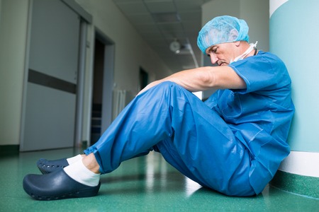 Sad surgeon sitting on floor in corridor at hospitalの写真素材