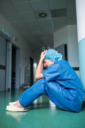 Sad surgeon sitting on floor in corridor at hospitalの写真素材