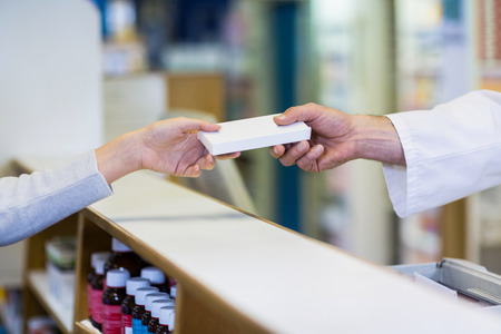 Pharmacist giving a box of medicine to customer in pharmacyの写真素材
