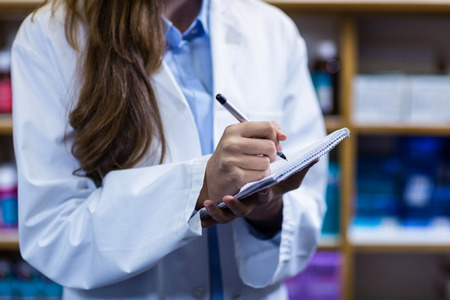 Mid-section of pharmacist writing on notepad in pharmacyの写真素材