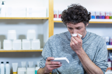 Customer checking medicine box while sneezing in pharmacyの写真素材