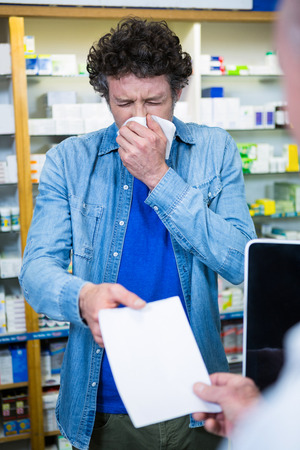 Customer sneezing while giving prescription to pharmacist in pharmacyの写真素材