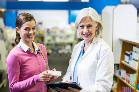 Portrait of pharmacist writing prescriptions for customer on clipboard in pharmacyの写真素材