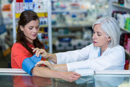 Pharmacist checking blood pressure of customer in pharmacyの写真素材