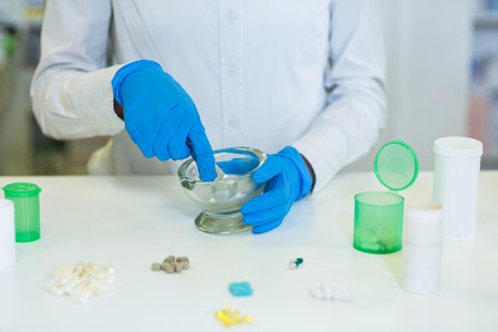 Mid-section of pharmacist grinding medicine in mortal and pestle at pharmacy