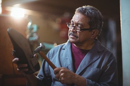 Shoemaker hammering on a shoe in workshopの写真素材