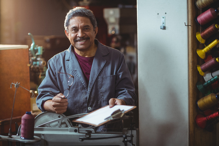Portrait of smiling shoemaker holding clipboard and spectacle in workshop
