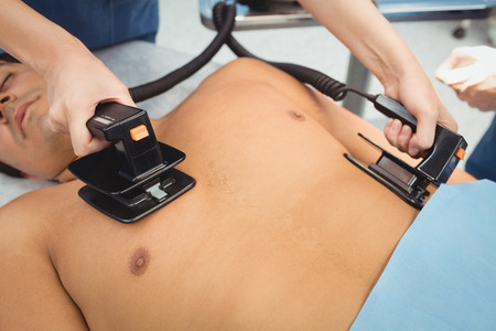 Female surgeon resuscitating an unconscious patient with a defibrillator at the hospitalの写真素材