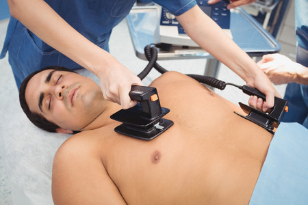 Female surgeon resuscitating an unconscious patient with a defibrillator at the hospitalの写真素材