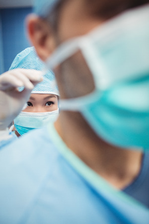 Close-up of nurse helping a surgeon in tying surgical mask in operation room at the hospitalの写真素材