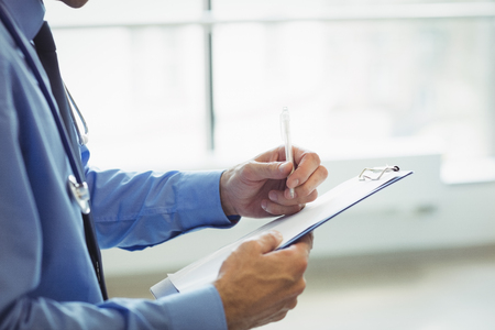 Mid section of doctor writing on clipboard at the hospitalの写真素材