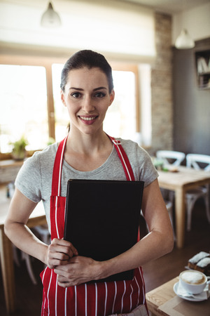 Portrait of female baker holding menu in bakery shopの写真素材