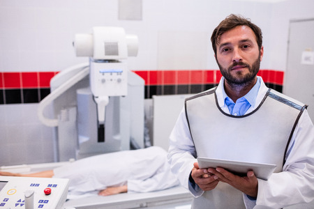 Portrait of doctor holding digital tablet and patient lying on x ray machine in hospital