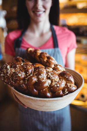 Mid-section of female baker holding freshly baked loaf of bread in bakery shopの写真素材