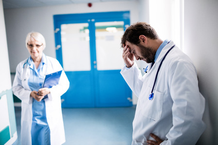 Sad doctor leaning against the wall in hospital corridorの写真素材