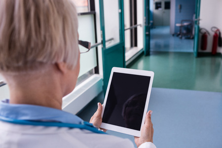 Rear view of doctor using digital tablet in hospital corridor