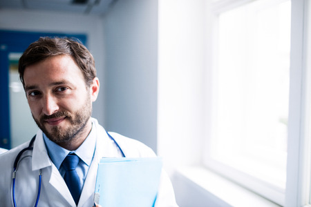 Portrait of a confident doctor with clipboard standing in the hospital corridor