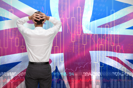 Businessman standing back to camera hands on head against digitally generated great britain national flagの写真素材