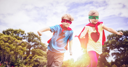 Playful siblings playing together while disguise as superhero against trees and plants growing at parkの写真素材