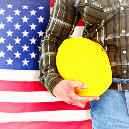 Manual worker holding helmet against rippled us flag