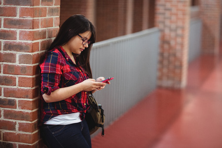 Female student using mobile phone in corridor at collegeの写真素材
