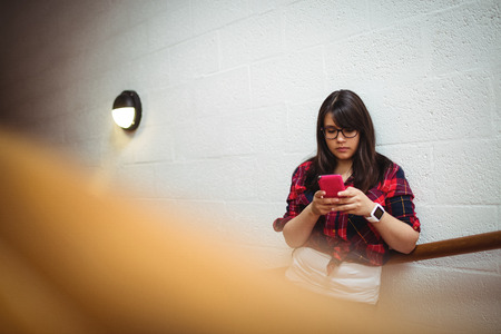 Female student using mobile phone in collegeの写真素材