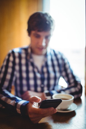 Student using mobile phone while having coffee in collegeの写真素材