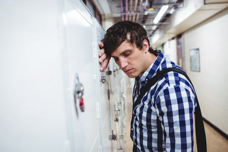 Sad student leaning on locker in collegeの写真素材